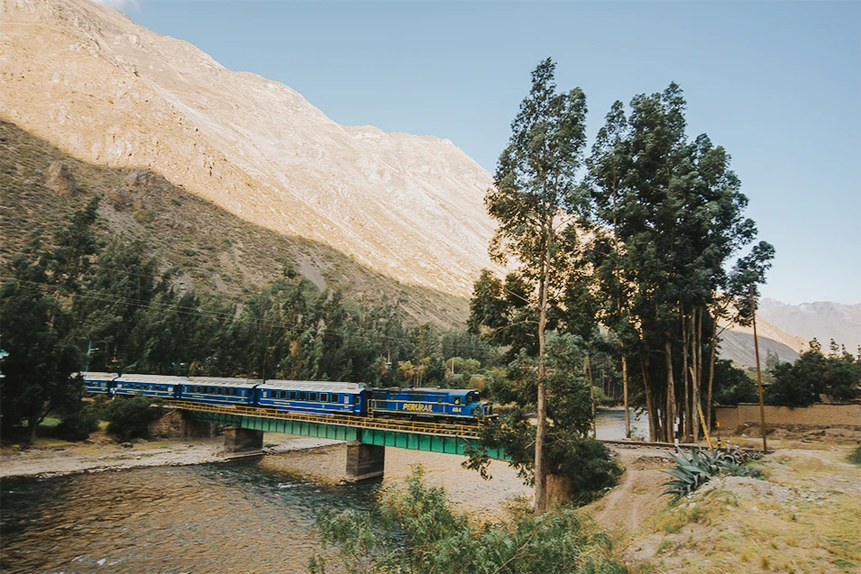 Expedition train crossing a scenic bridge with the Andes mountains in the background on the route to Machu Picchu. 