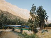Expedition train crossing a scenic bridge with the Andes mountains in the background on the route to Machu Picchu. 