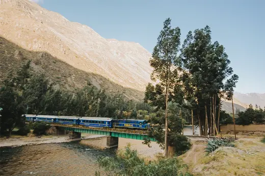Expedition train crossing a scenic bridge with the Andes mountains in the background on the route to Machu Picchu. 