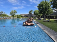 Guests relaxing by an infinity pool at a luxury resort on a sunny day in Bali, Indonesia. 