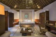 Spacious interior of a luxury Mayan-style villa with palapa roof, canopy bed, and natural wood furnishings in Mexico. 