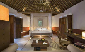 Spacious interior of a luxury Mayan-style villa with palapa roof, canopy bed, and natural wood furnishings in Mexico. 