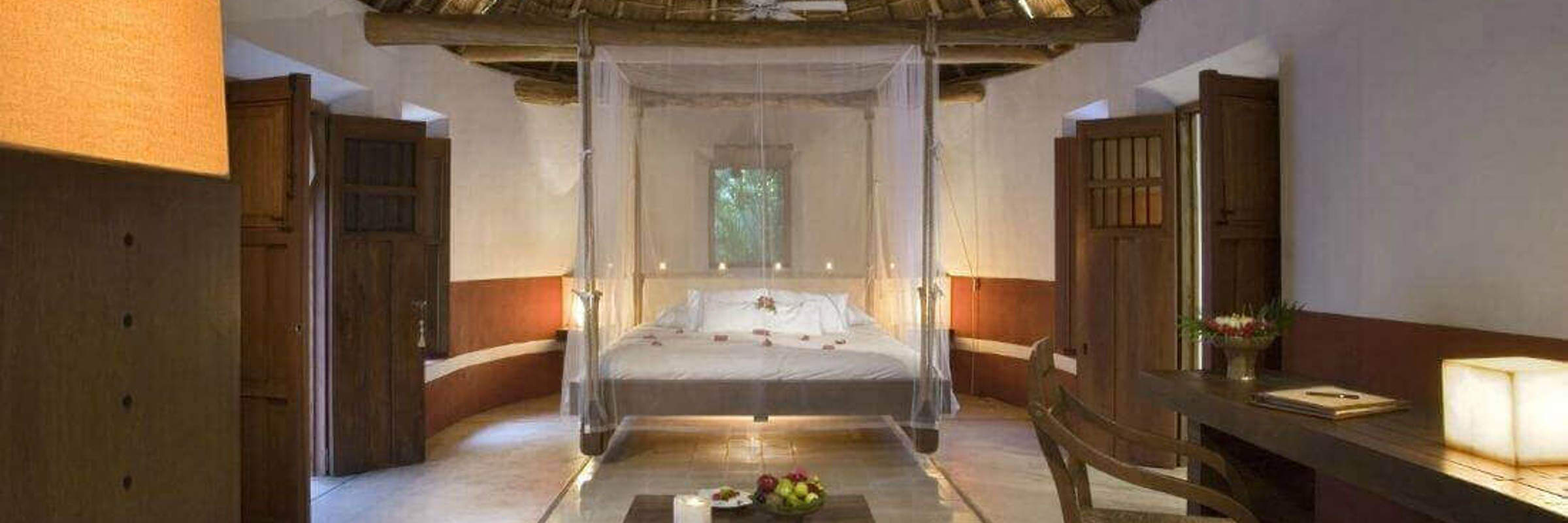 Spacious interior of a luxury Mayan-style villa with palapa roof, canopy bed, and natural wood furnishings in Mexico. 