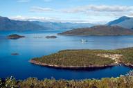 A cruise ship navigates the deep blue waters of Chile's fjords, weaving between lush green islands and distant Andean peaks. 