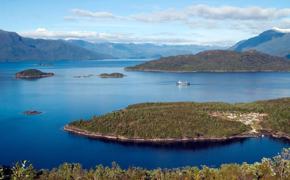 A cruise ship navigates the deep blue waters of Chile's fjords, weaving between lush green islands and distant Andean peaks. 