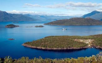 A cruise ship navigates the deep blue waters of Chile's fjords, weaving between lush green islands and distant Andean peaks. 