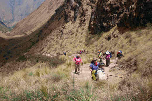 Hikers and porters trekking through a high mountain pass on the Inca Trail in Peru's Sacred Valley. 