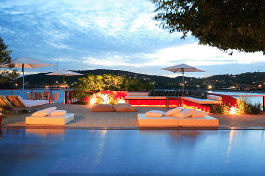 Evening view of the illuminated pool at Alta Insolito Boutique Hotel in Buzios, with scenic ocean and sunset backdrop. 