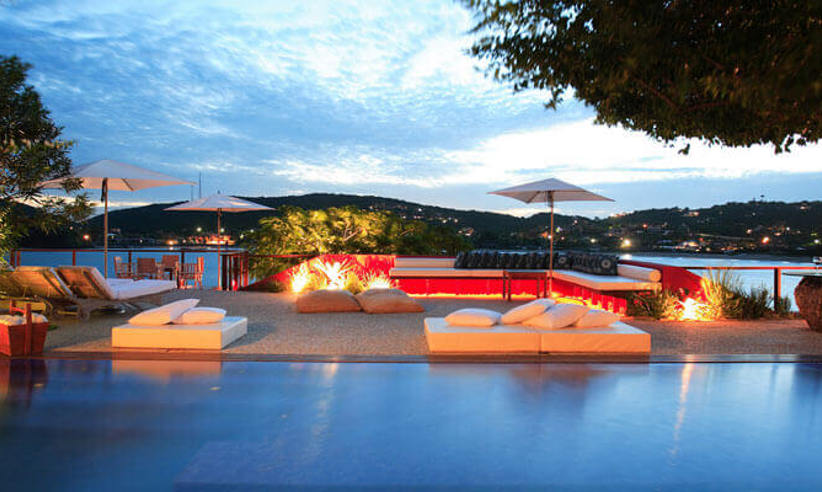 Evening view of the illuminated pool at Alta Insolito Boutique Hotel in Buzios, with scenic ocean and sunset backdrop. 