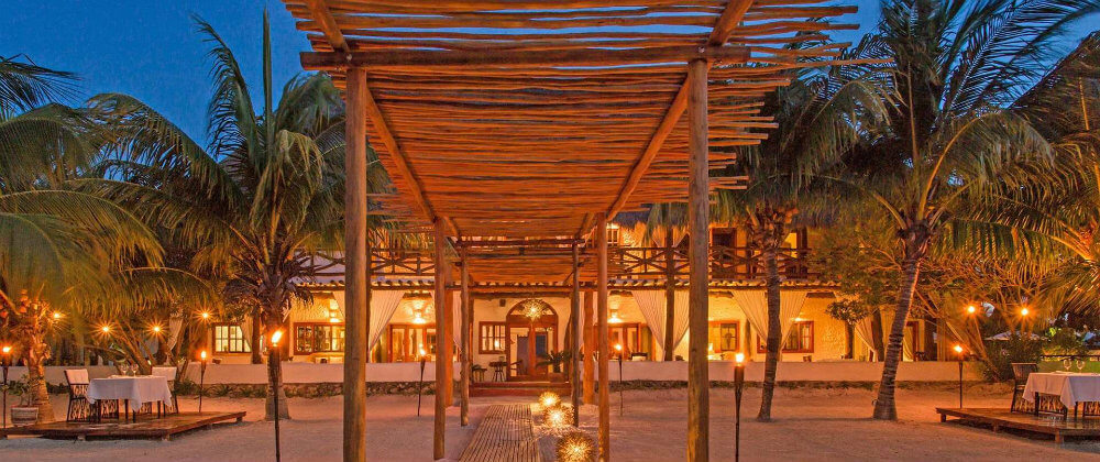 Evening view of Casa Sandra's open-air lounge and dining area on Holbox Island, with warm lighting and tropical surroundings. 