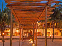 Evening view of Casa Sandra's open-air lounge and dining area on Holbox Island, with warm lighting and tropical surroundings. 