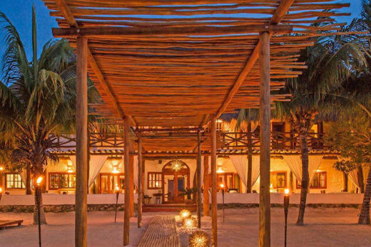 Evening view of Casa Sandra's open-air lounge and dining area on Holbox Island, with warm lighting and tropical surroundings. 