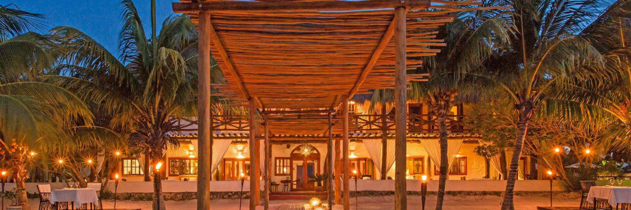 Evening view of Casa Sandra's open-air lounge and dining area on Holbox Island, with warm lighting and tropical surroundings. 