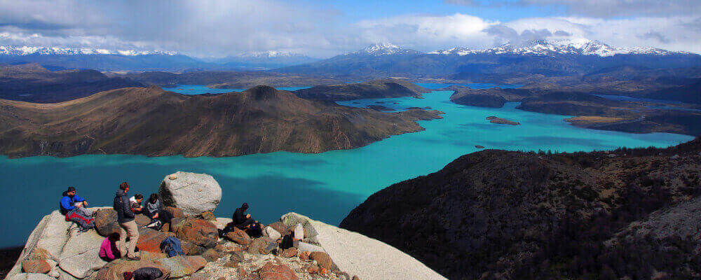 Hikers rest atop the Cuernos Trail with panoramic views of turquoise lakes and snow-capped peaks in Torres del Paine. 