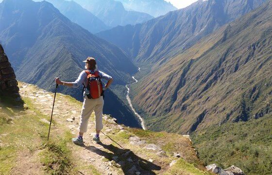 A hiker stands triumphantly atop the Andes, overlooking the Sacred Valley's endless ridges. 