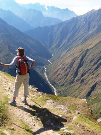 A hiker stands triumphantly atop the Andes, overlooking the Sacred Valley's endless ridges. 