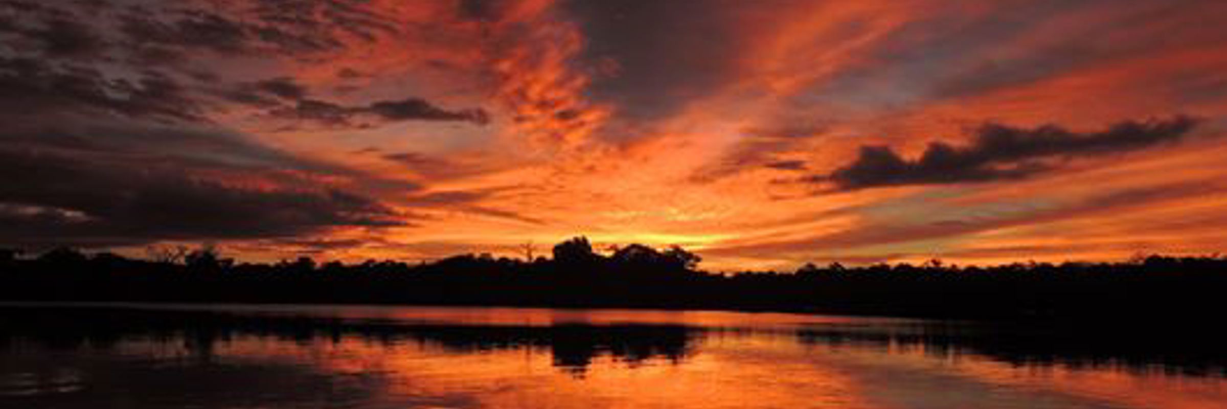 Stunning sunrise over the Amazon River, with vibrant orange and red hues reflecting across the calm water. 