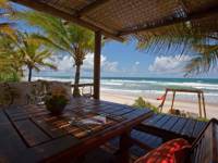 Table with ocean view at beachfront restaurant in Bahia, Brazil, shaded by palm trees and thatch roof. 