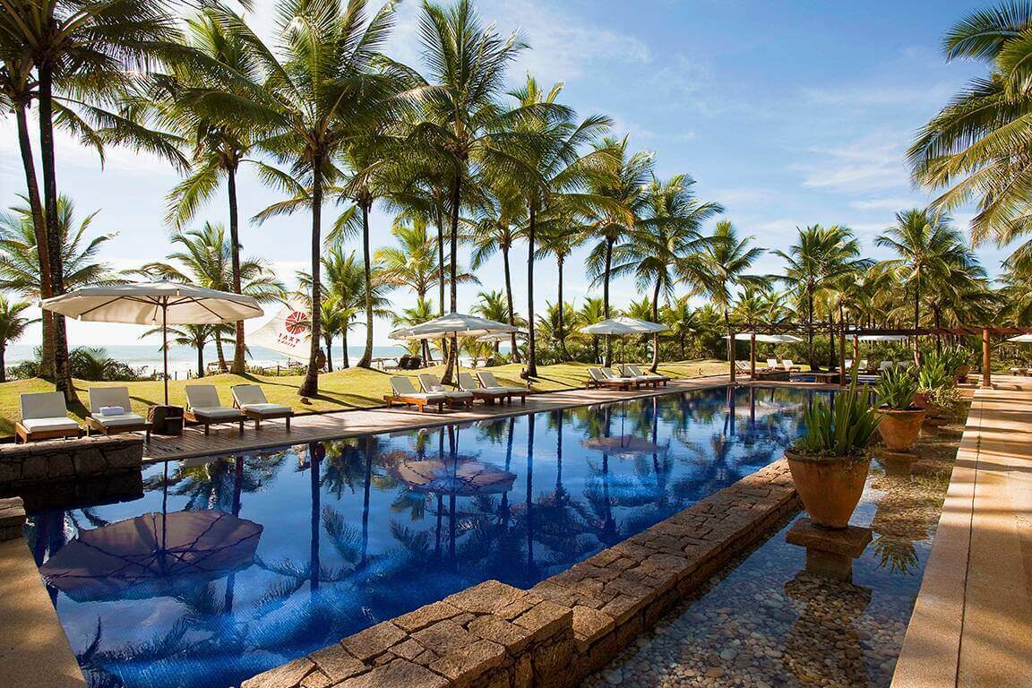 Tropical poolside with palm trees, sun loungers, and blue sky at UXUA Hotel in Trancoso, Bahia, Brazil. 