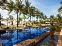 Tropical poolside with palm trees, sun loungers, and blue sky at UXUA Hotel in Trancoso, Bahia, Brazil. 