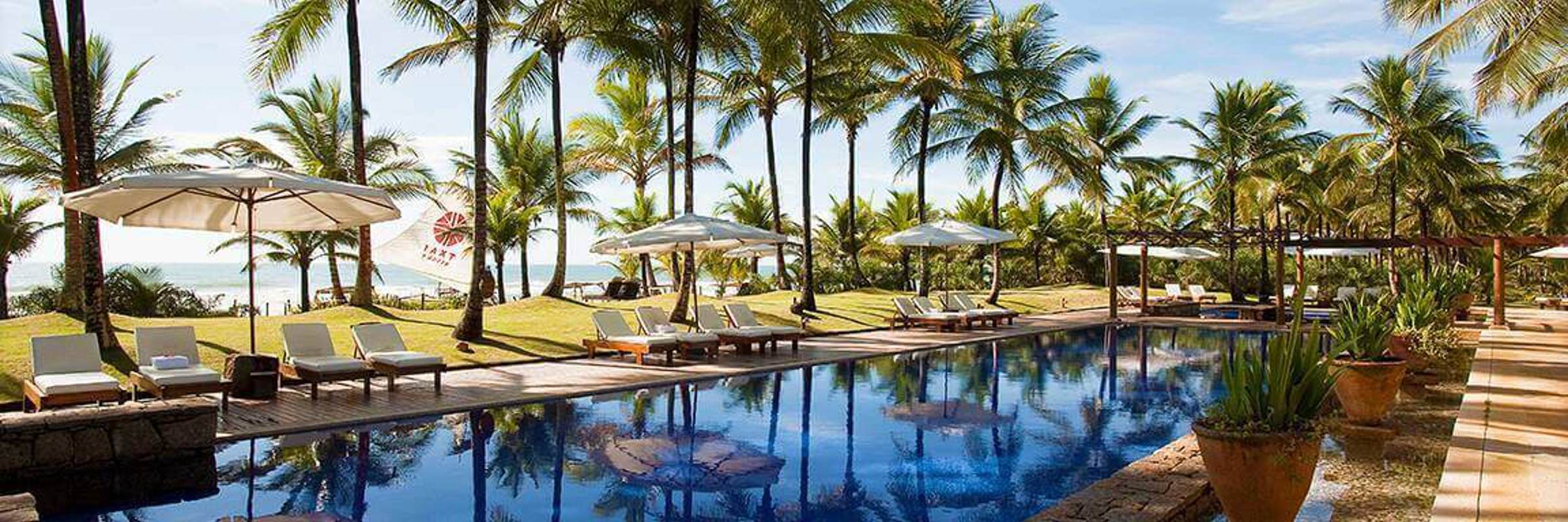 Tropical poolside with palm trees, sun loungers, and blue sky at UXUA Hotel in Trancoso, Bahia, Brazil. 