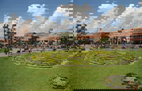 Plaza de Armas in Cusco with manicured gardens and the historic cathedral under blue skies. 