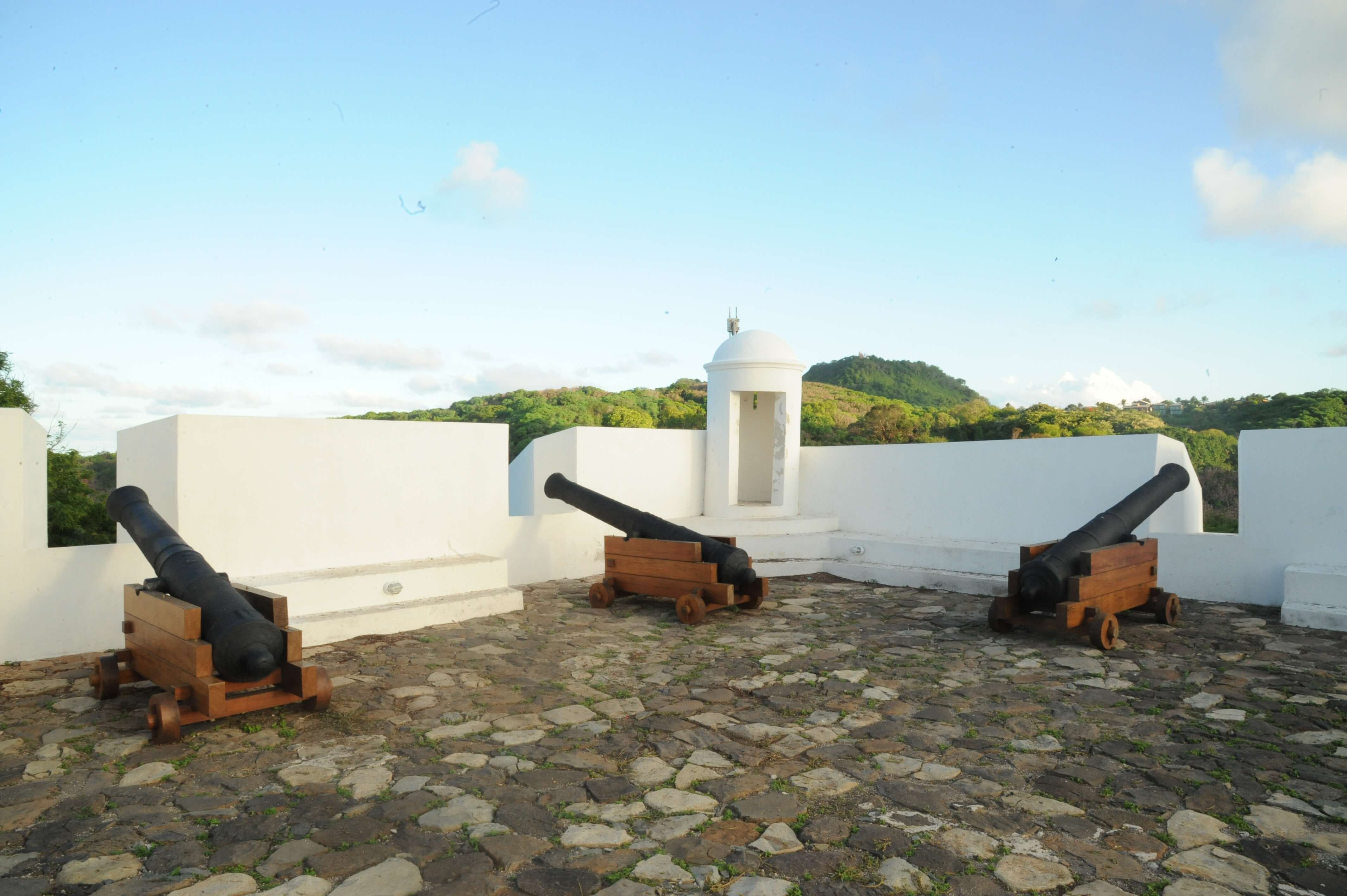Historic cannons at Noronha Fort overlooking the coastline of Fernando de Noronha, Brazil, under clear blue skies. 