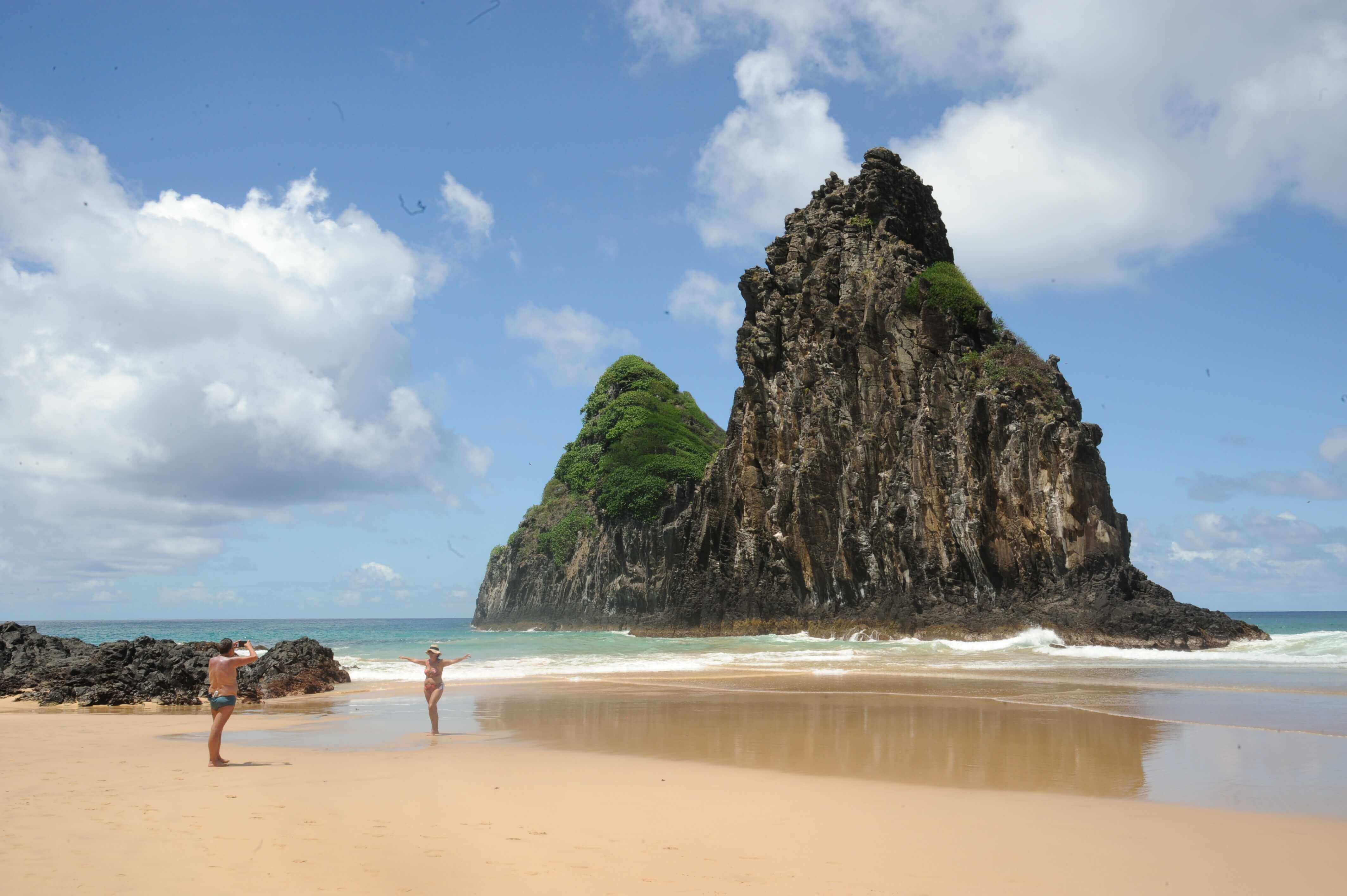 Couple on a beach in Fernando de Noronha with the iconic Two Brothers Rocks rising in the background. 