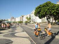 People cycling along the iconic Copacabana promenade with its wave-patterned pavement in Rio de Janeiro, Brazil. 
