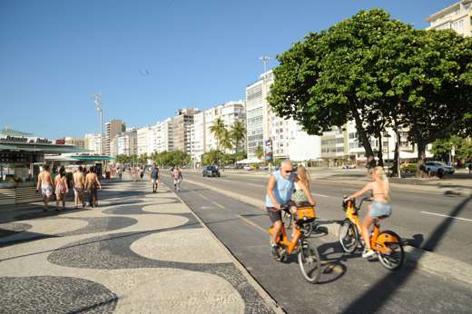 People cycling along the iconic Copacabana promenade with its wave-patterned pavement in Rio de Janeiro, Brazil. 