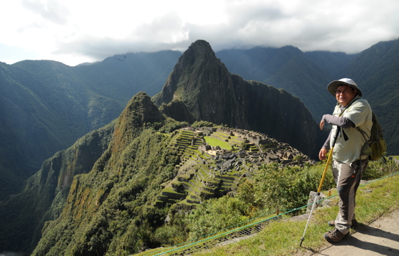 Guide standing above Machu Picchu with panoramic views of the Inca ruins and Andes Mountains. 