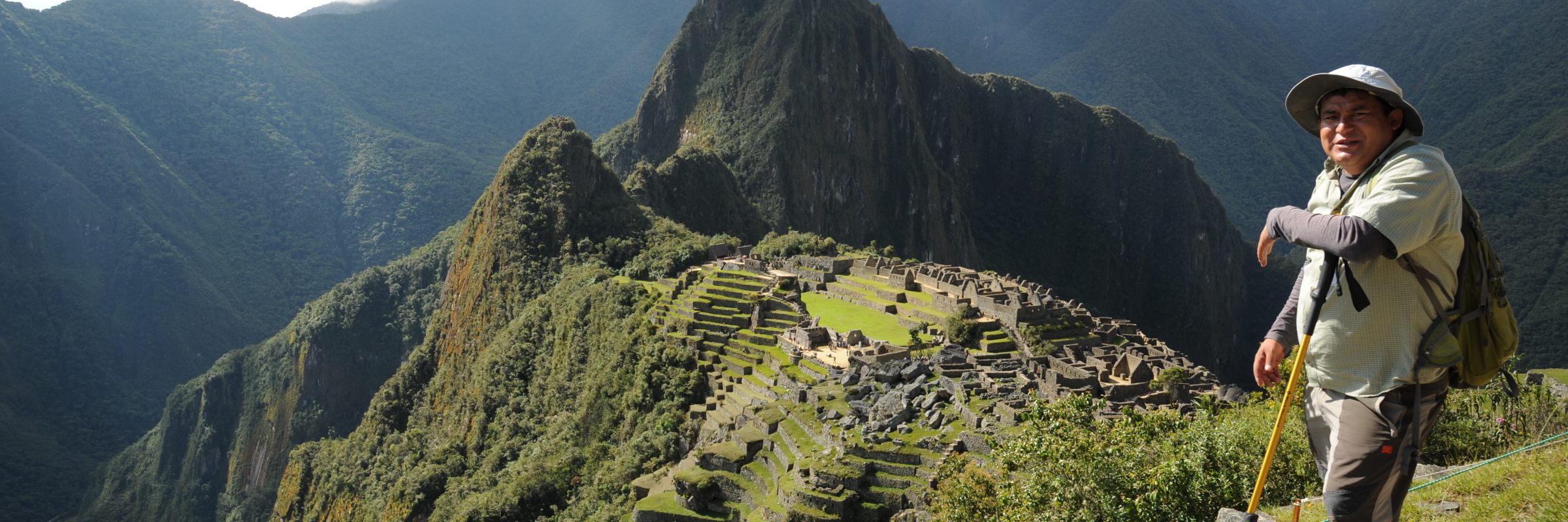 Guide standing above Machu Picchu with panoramic views of the Inca ruins and Andes Mountains. 