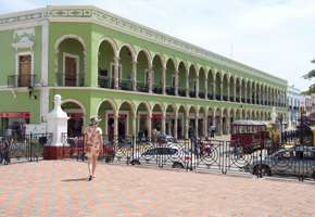 Historic green arcade building on Merida's Plaza Grande, Yucatan, with colonial arches, statue, and pedestrian view. 