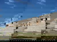 Visitors explore Uxmal's grand Mayan ruins in Yucatan, surrounded by lush jungle and ancient stone architecture. 