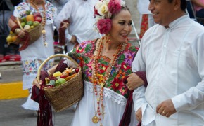 Couple in traditional Yucatan folk costumes dancing during a colourful festival in Mexico, with musicians in the background. 