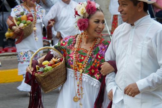 Couple in traditional Yucatan folk costumes dancing during a colourful festival in Mexico, with musicians in the background. 
