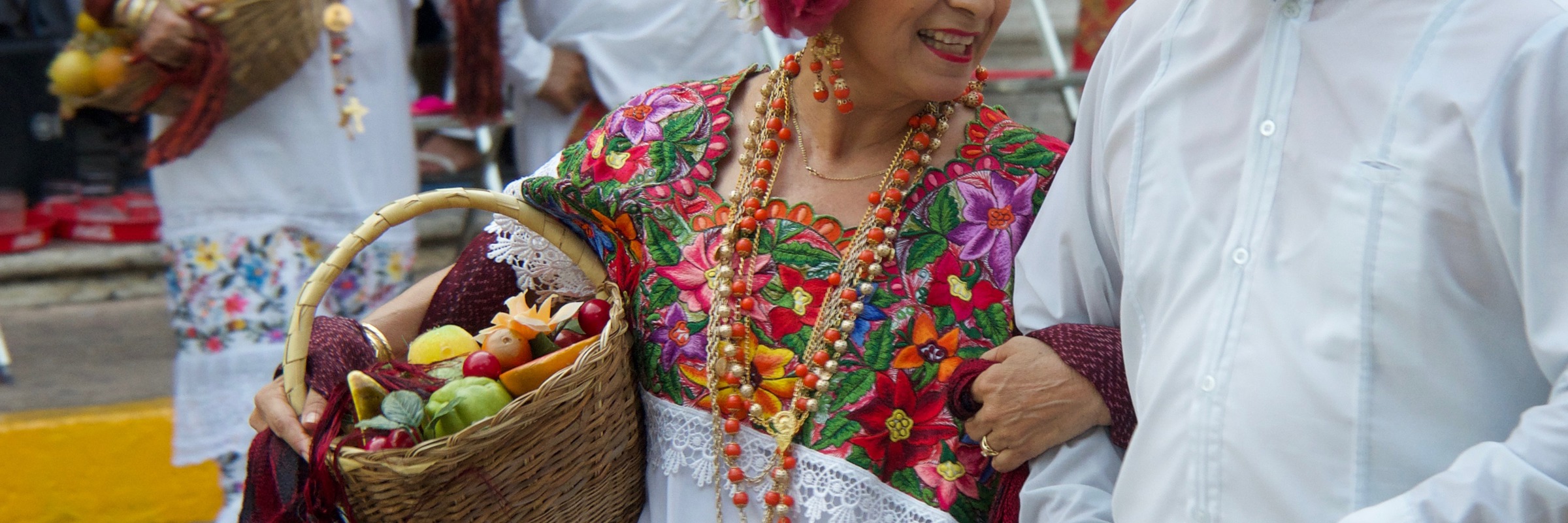 Couple in traditional Yucatan folk costumes dancing during a colourful festival in Mexico, with musicians in the background. 