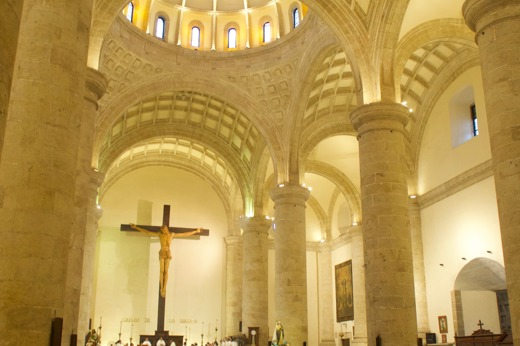 Interior of the Cathedral of Merida, Yucatan, with worshipers gathered beneath soaring arches and a large crucifix. 