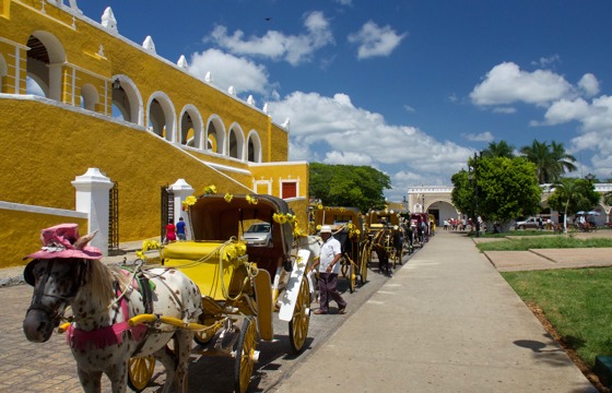 Colourful horse-drawn carriages lined up in front of the yellow Convent of San Antonio de Padua in Izamal, Yucatan, Mexico.