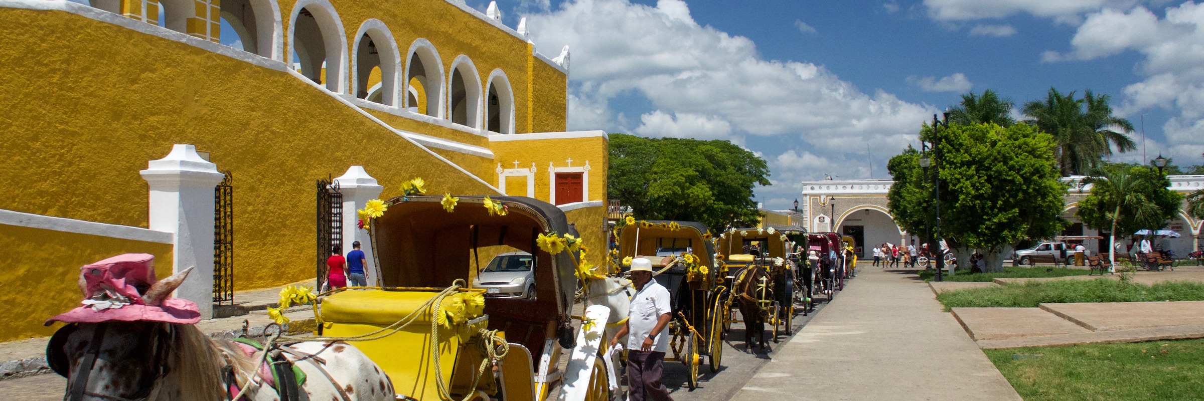 Colourful horse-drawn carriages lined up in front of the yellow Convent of San Antonio de Padua in Izamal, Yucatan, Mexico.