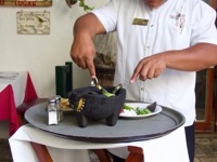 Server prepares fresh guacamole tableside using a traditional molcajete at a Mexican restaurant. 