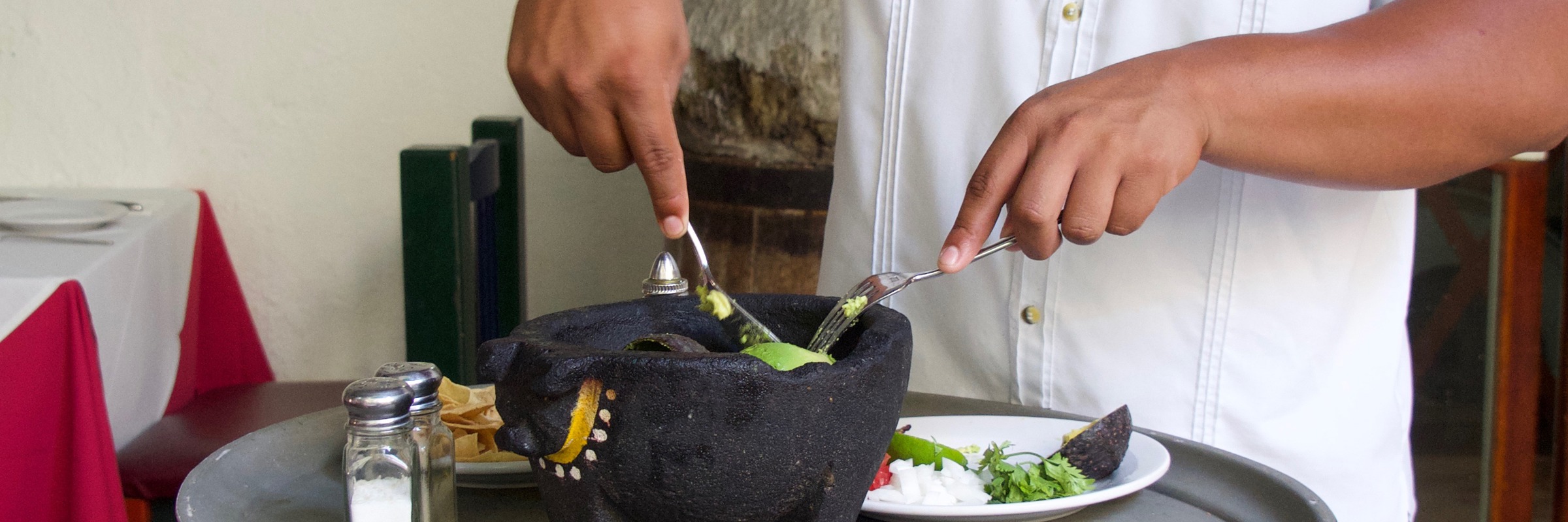 Server prepares fresh guacamole tableside using a traditional molcajete at a Mexican restaurant. 