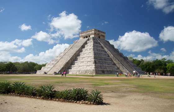 The Temple of Kukulcan at Chichen Itza rises under a bright sky, showcasing ancient Mayan architectural brilliance. 
