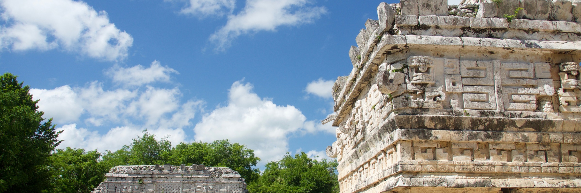 Mayan stone temples at Chichen Itza, including the Temple of the Skulls, set under a blue sky with scattered clouds in Yucatan, Mexico. 