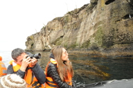 Two cruise passengers in a Zodiac take photos of dramatic coastal cliffs during a  Patagonia expedition in Chile. 