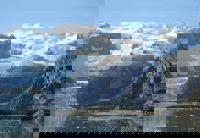 Towering snow-covered peaks and massive glaciers rise above icy blue waters in the wild Patagonian fjords of Chile. 