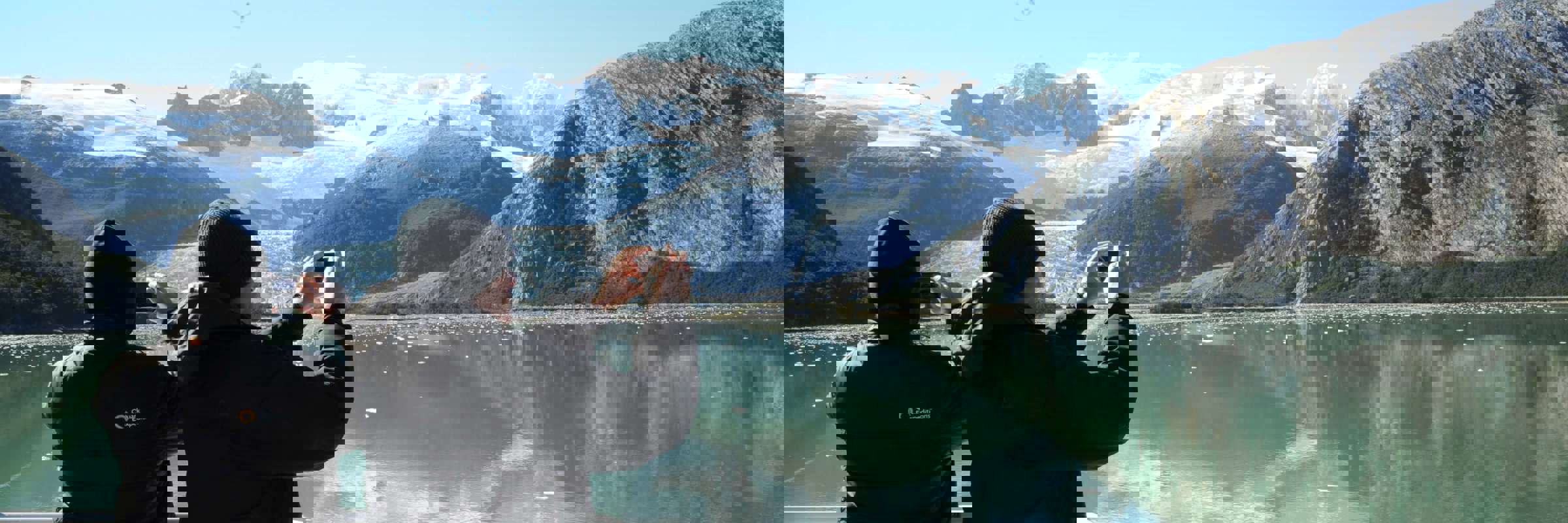 Two passengers photograph stunning glaciers and snow-capped peaks from the deck of a cruise ship in Chilean Patagonia. 