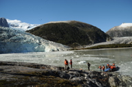 Cruise passengers in life vests explore the rocky glacier shoreline in Chilean Patagonia under clear blue skies. 