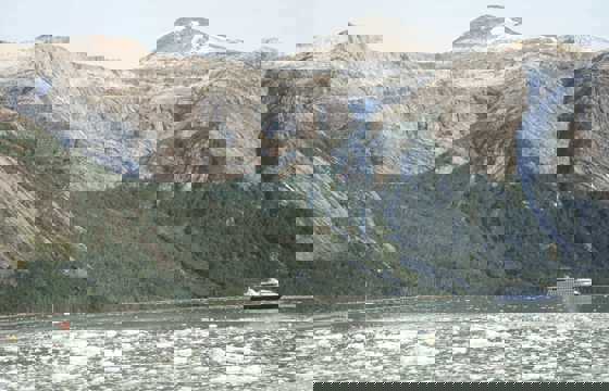 An expedition cruise ship navigates icy Patagonia waters beneath towering, rugged mountains in Chile's southern fjords. 