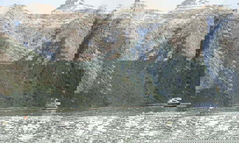 An expedition cruise ship navigates icy Patagonia waters beneath towering, rugged mountains in Chile's southern fjords. 